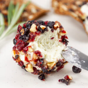 square crop of a blue cheese ball with a spreader knife in it.