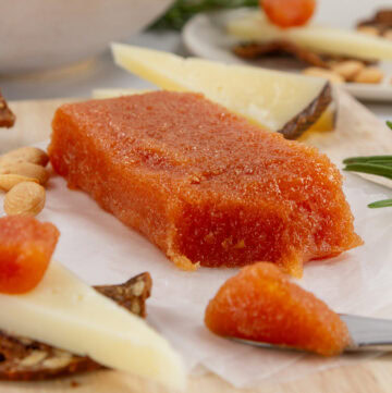square crop of a cube of quince paste on a cheese plate with a spreader.