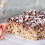 square crop of a Peppermint Rice Krispies Treats topped with chocolate and peppermint candies on a white plate with a candy can next to it.
