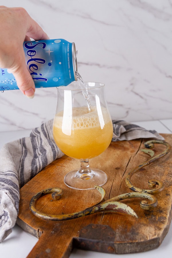 pouring sparkling water into a glass with ginger syrup to make a homemade ginger ale.