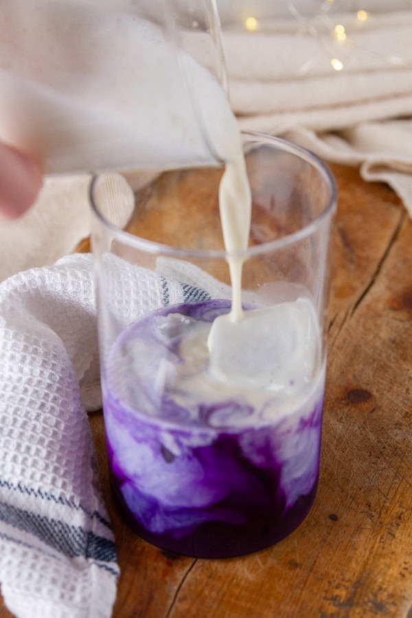 pouring milk into a glass with ube already in it.