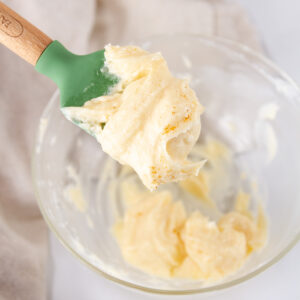 square crop of a small bowl with mayo and butter in it and a green spatula with some spread on it.