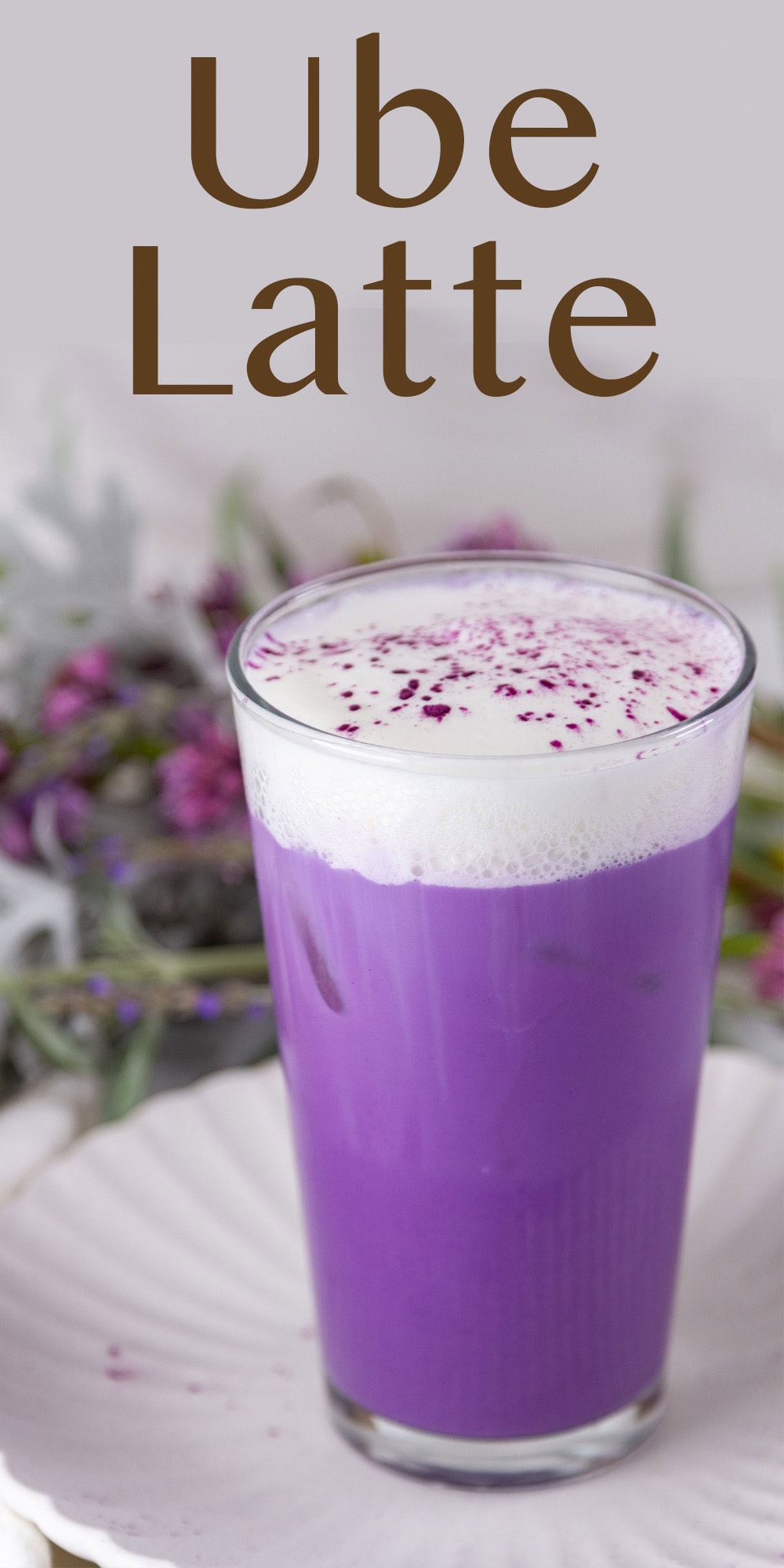 a pretty purple iced ube latte in a glass in front of some flowers.