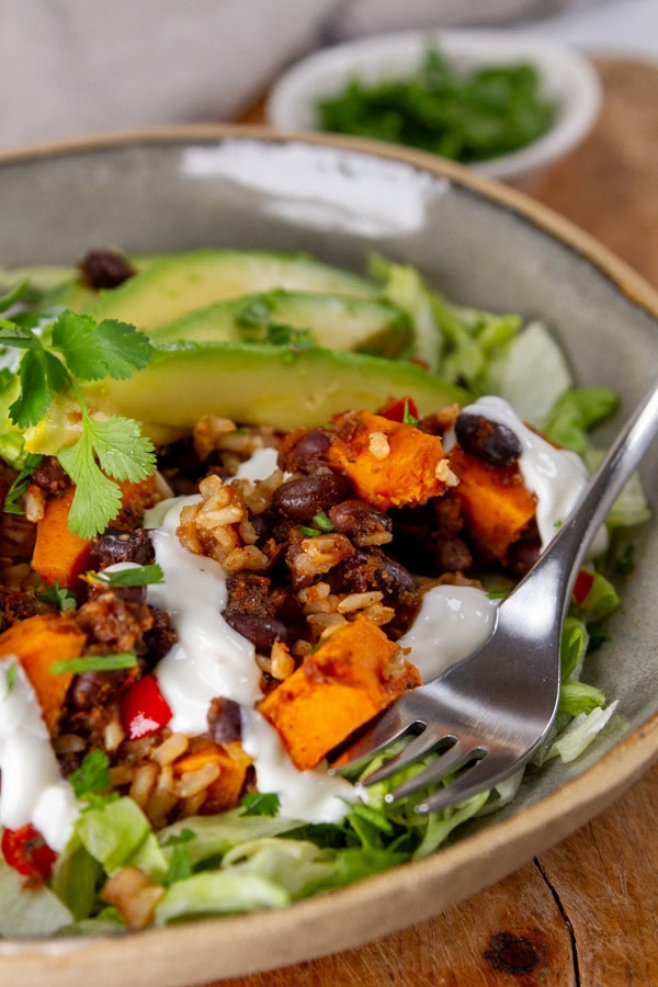 looking at the side of a bowl filled with grains, veggies, and beans.