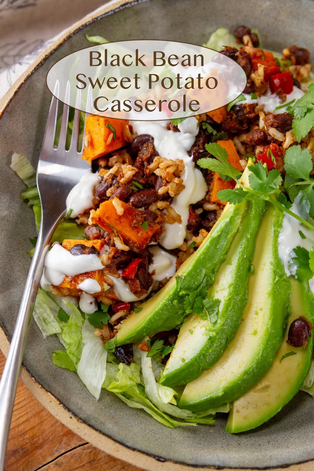 a bowl filled with black bean and sweet potato casserole topped with avocado and sour cream and a fork in the bowl.