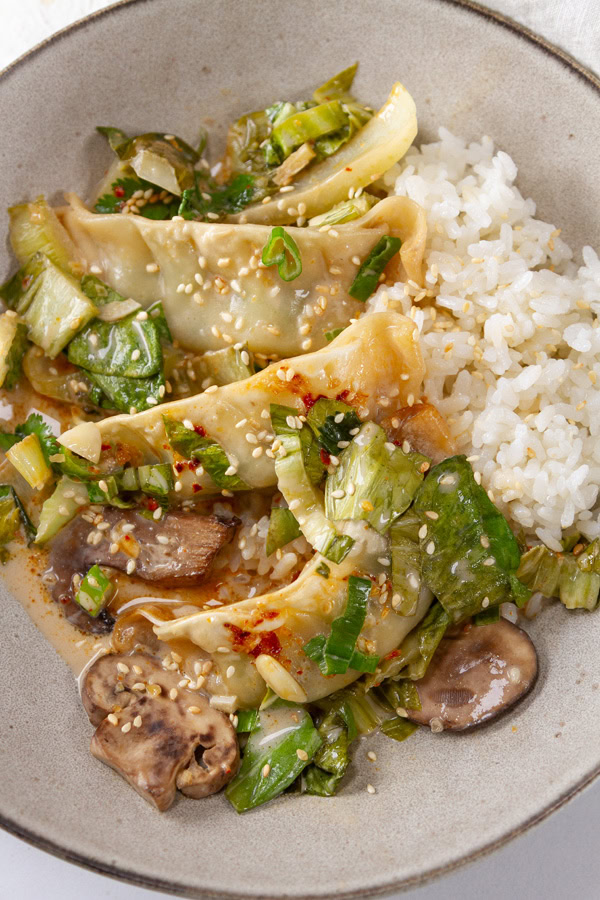 dumplings, veggies, and sauce served with rice in a bowl.