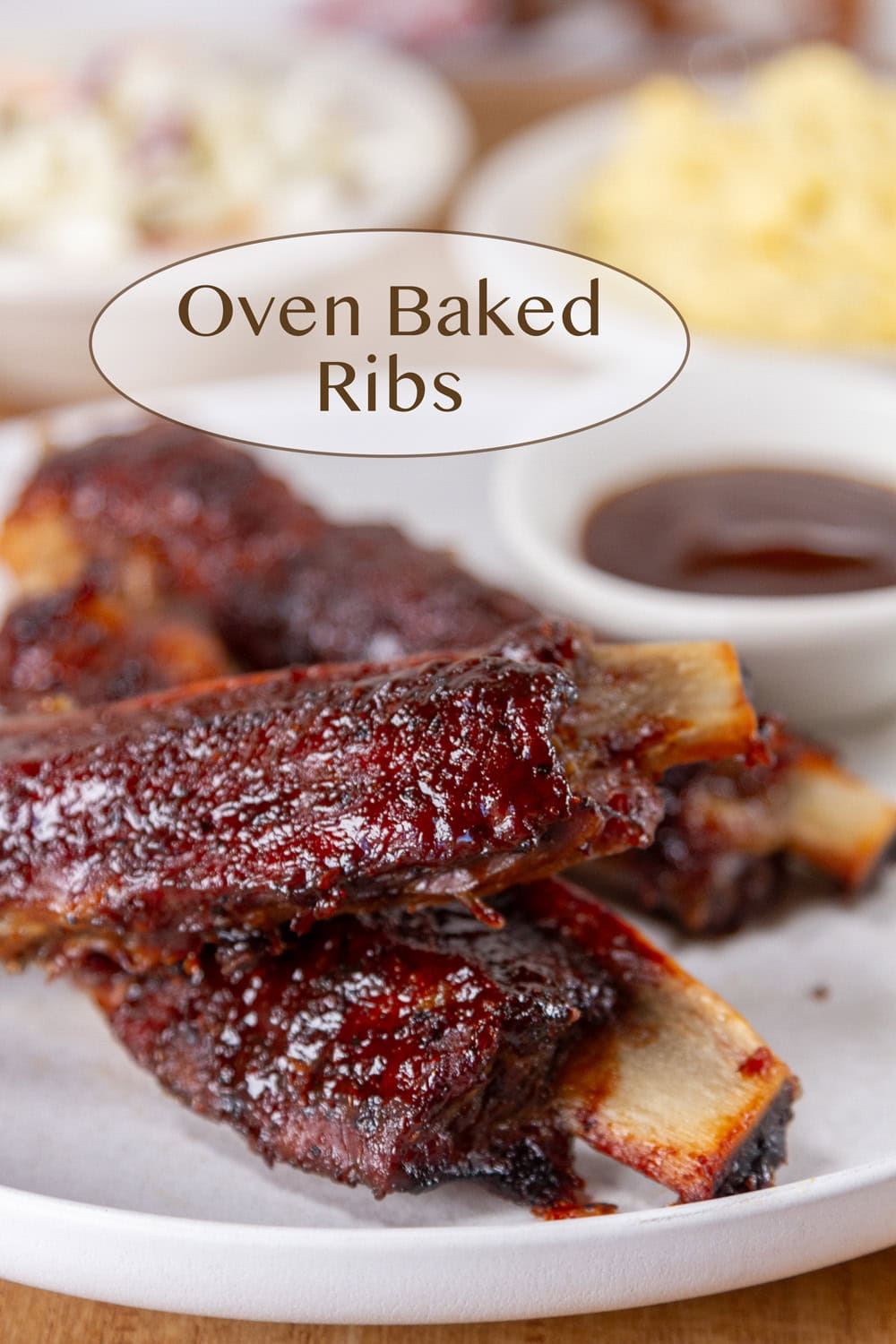 ribs piled on a plate with BBQ sauce, potato salad, and coleslaw in the background.