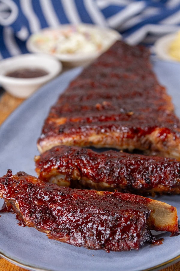 baked ribs on a blue serving plate with a blue striped cloth and side dishes in the background.