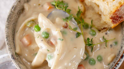 square crop of a cup of noodle soup with a spoonful being taken out and a chunk of bread in the upper right.