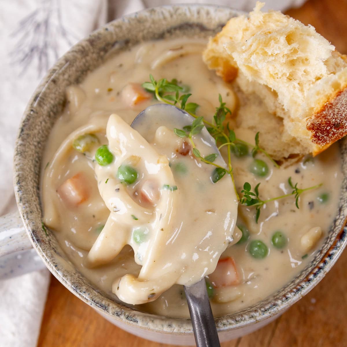 square crop of a cup of noodle soup with a spoonful being taken out and a chunk of bread in the upper right.