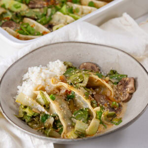 square crop of a serving of dumplings on a plate in sauce in front of the casserole dish.