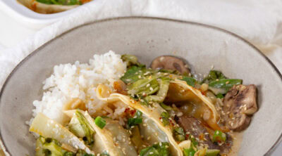 square crop of a serving of dumplings on a plate in sauce in front of the casserole dish.