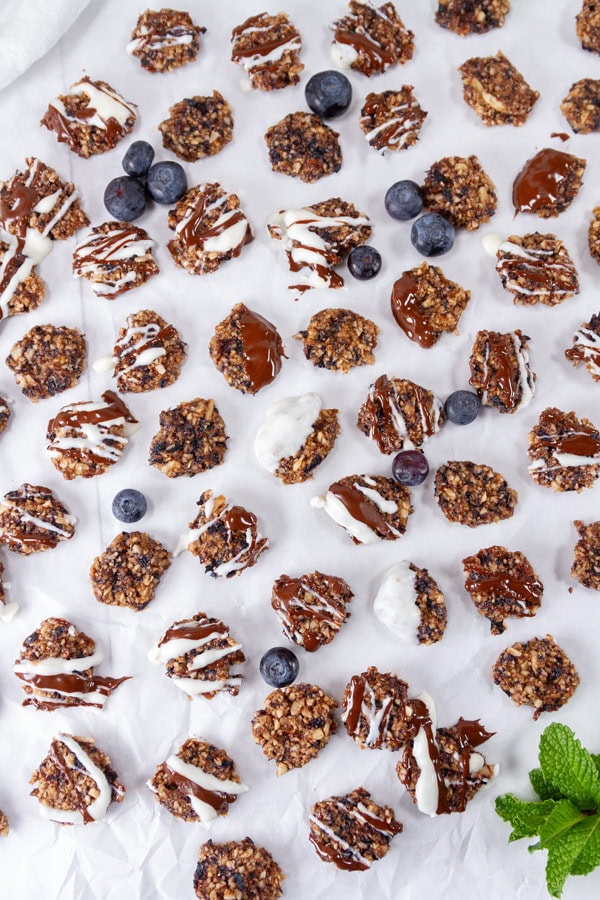 a lot of little cookies with blueberries and some mint on a large piece of white parchment paper.