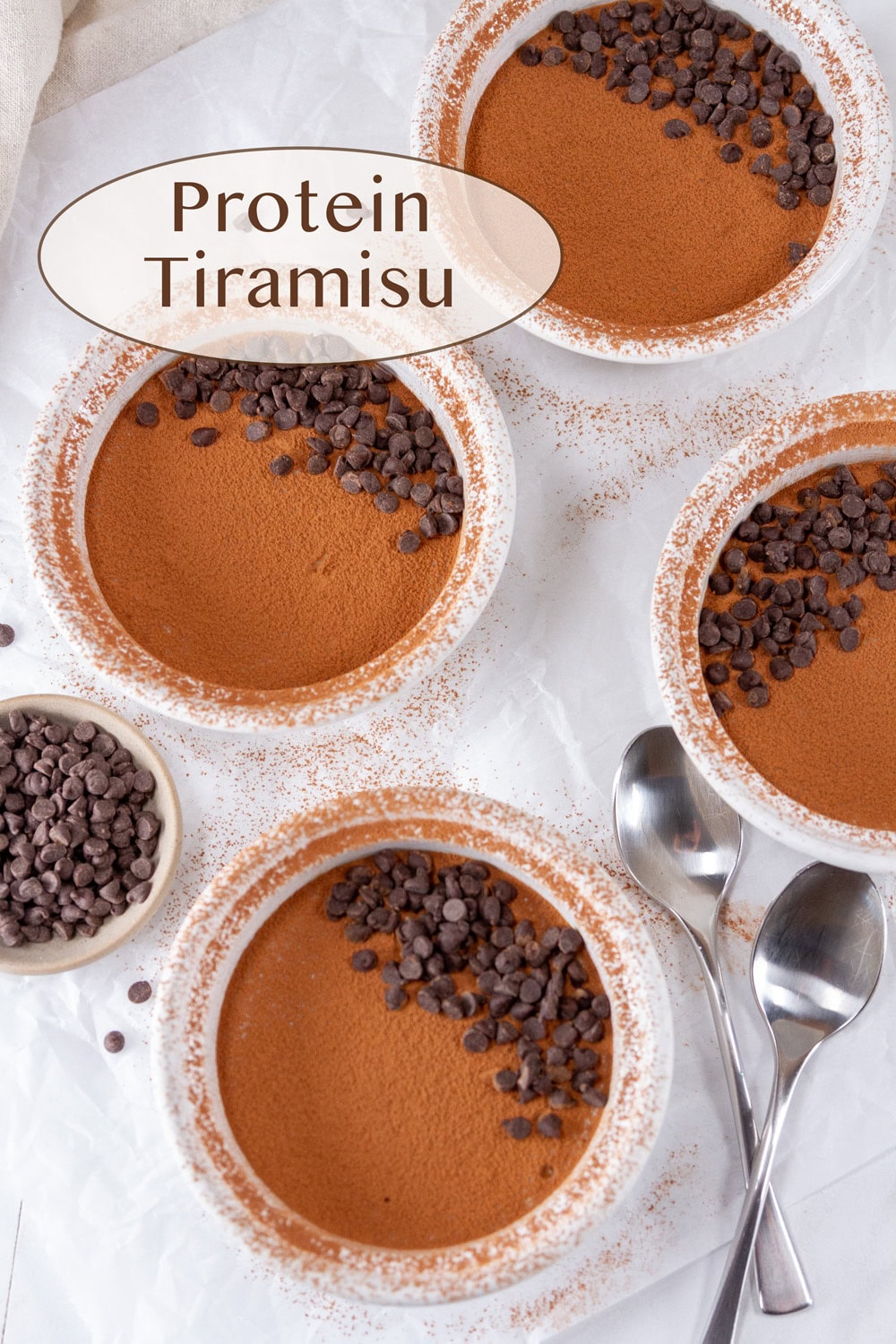 4 bowls of tiramisu with some spoons and chocolate chips around them.
