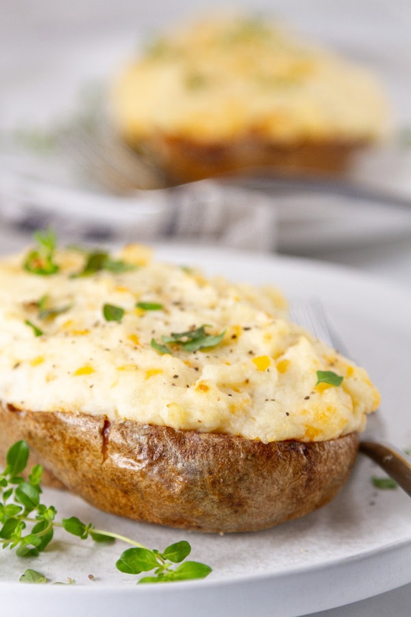 two baked stuffed potatoes on white plate garnished with fresh thyme.