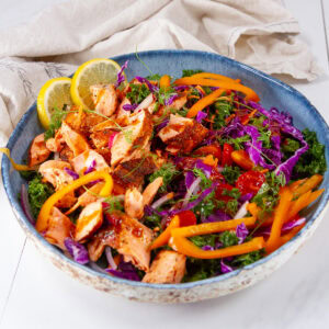 square crop of a kale salad with cooked salmon on top in a blue bowl.