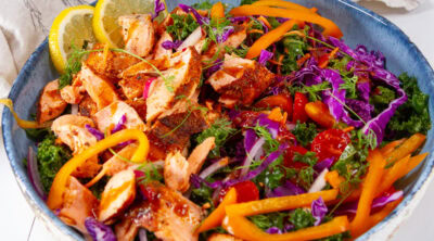 square crop of a kale salad with cooked salmon on top in a blue bowl.