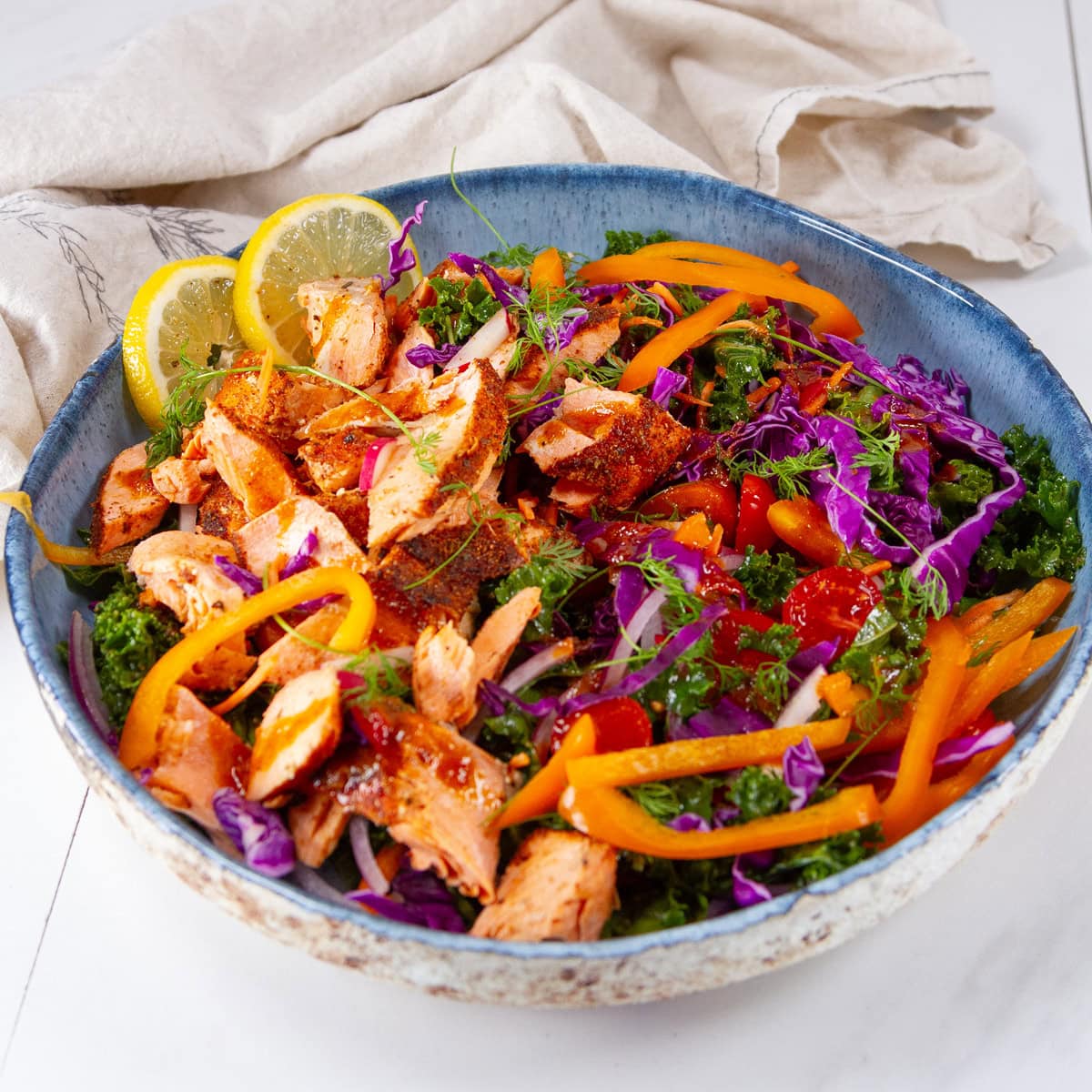 square crop of a kale salad with cooked salmon on top in a blue bowl.