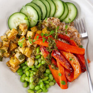 square crop of a bowl with grains, tofu, and veggies and a fork to the right.