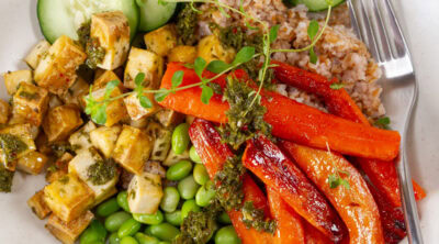 square crop of a bowl with grains, tofu, and veggies and a fork to the right.