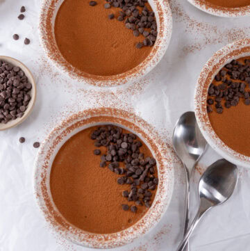 square crop of ramekins of tiramisu with some spoons around.