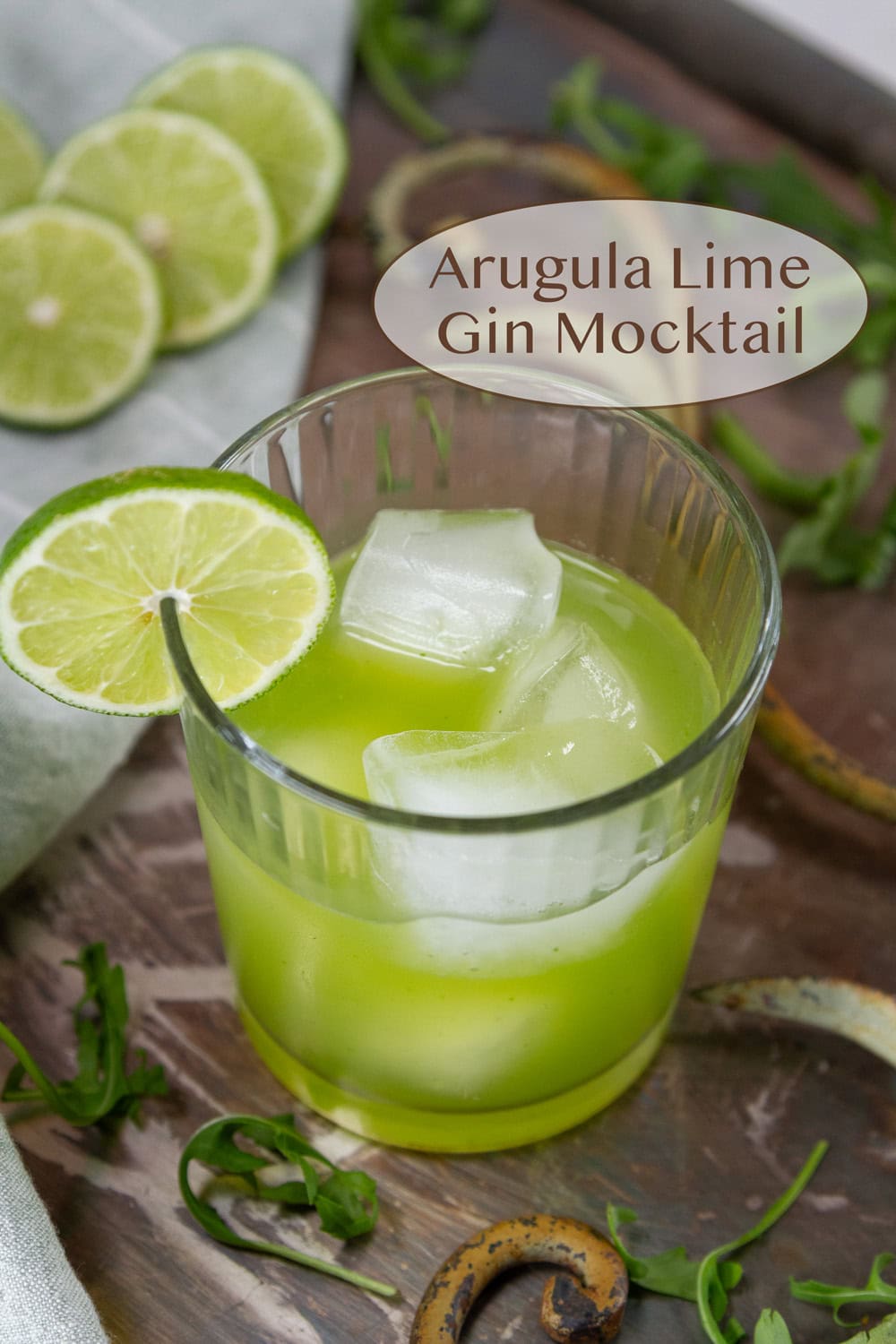 a glass filled with green drink over ice and some lime slices in the background.