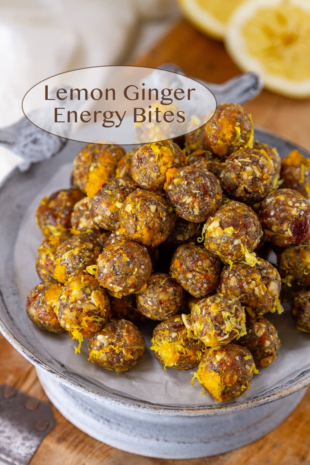 lemon ginger bites stacked up on a metal serving plate with lemons in the background.
