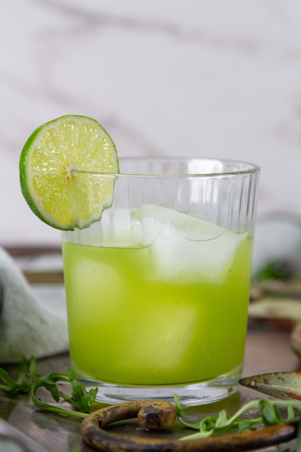 looking at the side of a glass filled with ice and green mocktail drink garnished with a lime slice.