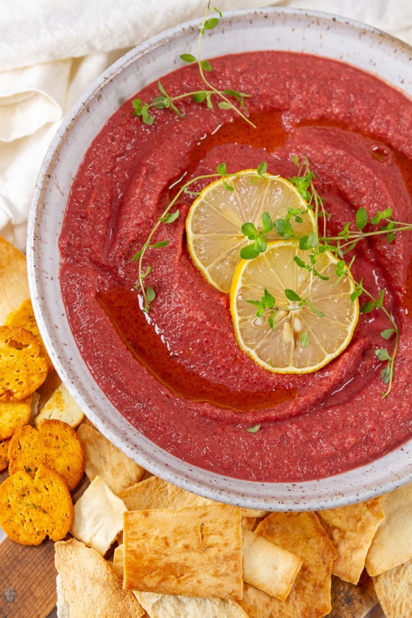 a large white bowl filled with flavored hummus garnished with lemon slices and chips next to the bowl.