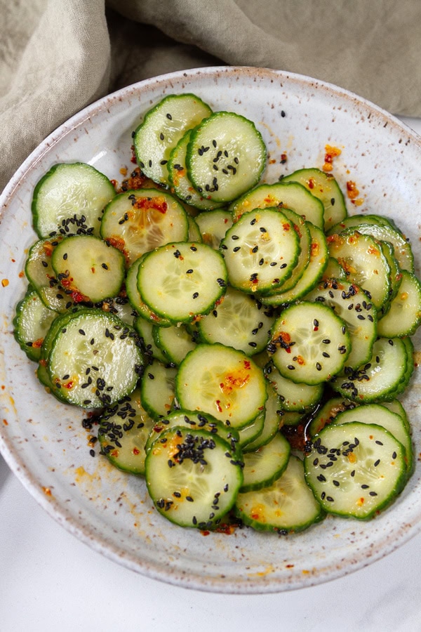 sliced cucumbers in dressing in a white bowl with a cloth napkin in the upper left.