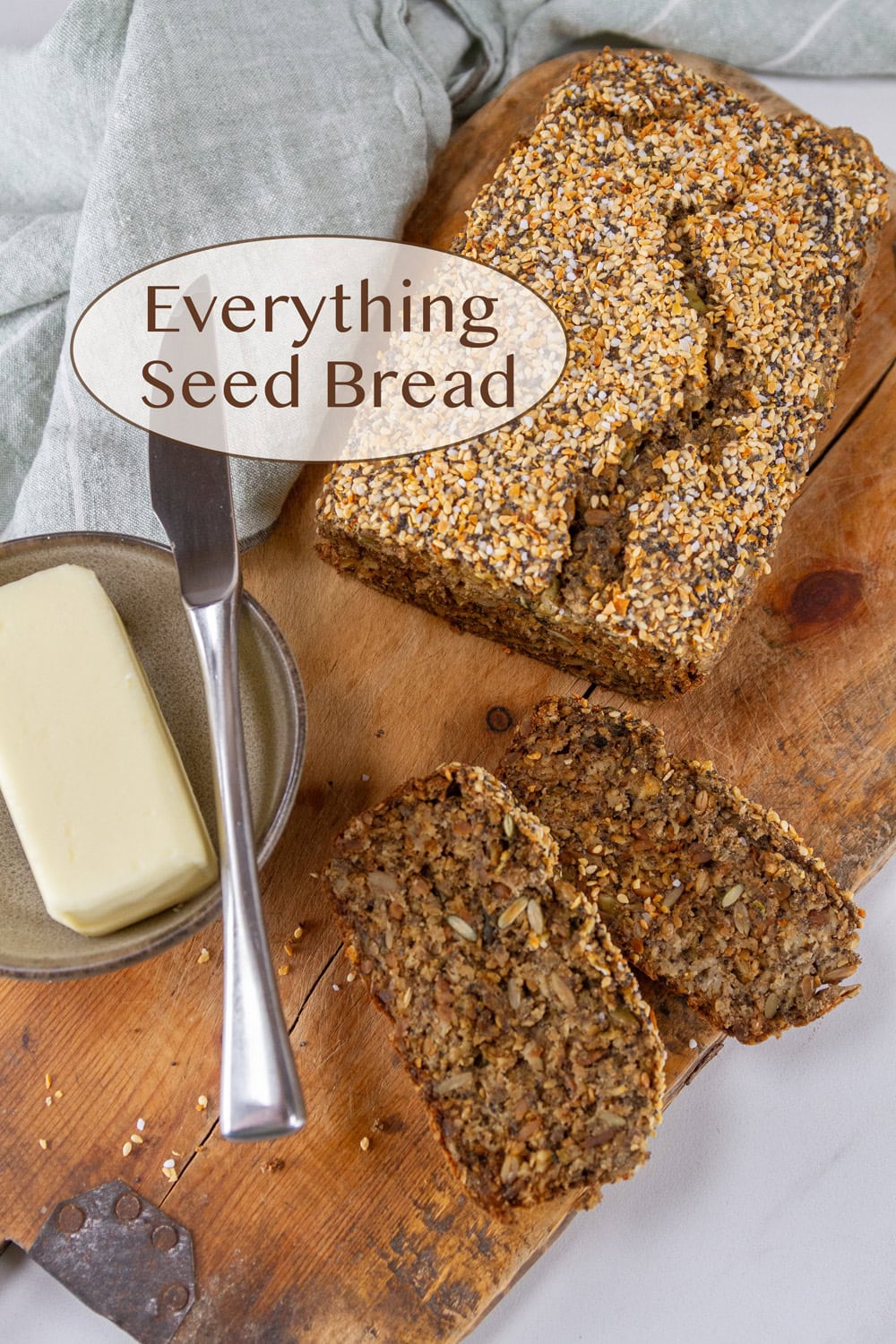 a loaf of everything seed bread on a wooden cutting board with some butter and a knife.