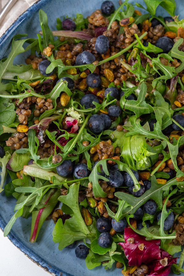 salad with lentils blueberries and pistachios in a blue bowl.