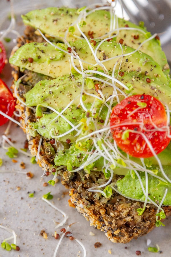 avocado toast on seed bread with sprouts and cherry tomatoes.