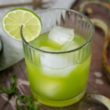 square crop of a glass filled with arugula lime gin mocktail and garnished with a lime slice.