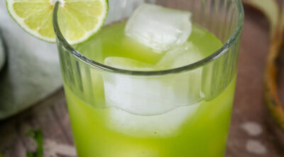 square crop of a glass filled with arugula lime gin mocktail and garnished with a lime slice.