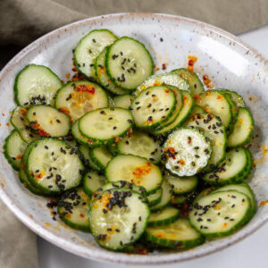 square crop of a white bowl filled with sliced cucumbers in sesame dressing.