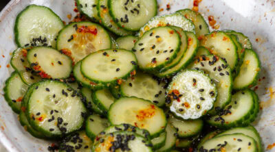 square crop of a white bowl filled with sliced cucumbers in sesame dressing.