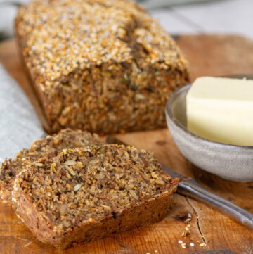 square crop of a loaf of seed bread with some slices in front and a small dish of butter.