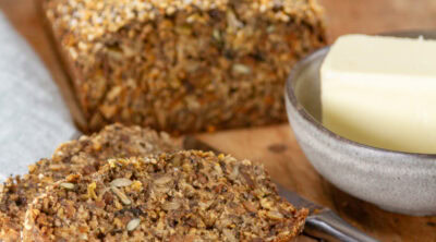 square crop of a loaf of seed bread with some slices in front and a small dish of butter.
