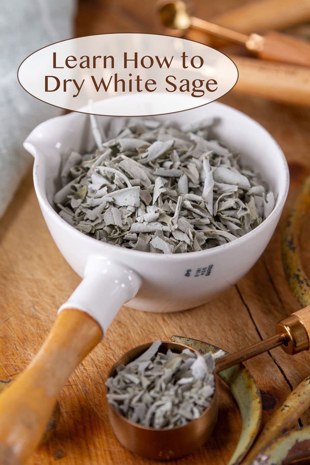 a white measuring cup filled with dried sage and a tablespoon next to it on a wooden cutting board.