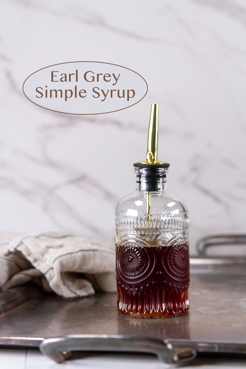 a glass bottle filled with earl grey simple syrup on a silver tray.