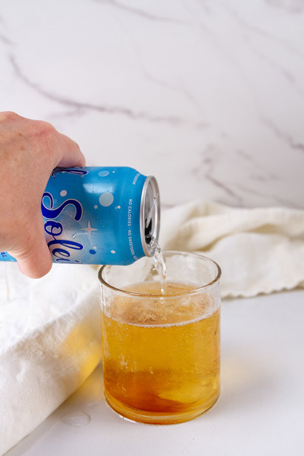 adding sparkling water to Earl Grey syrup in a glass.