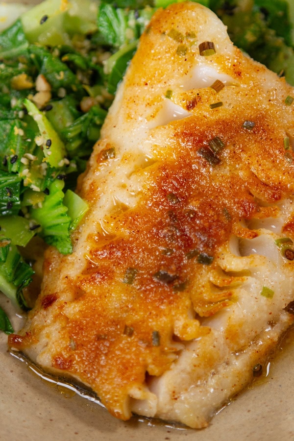 a piece of cooked black cod with maple garlic spice mix coating next to some cooked bok choy.