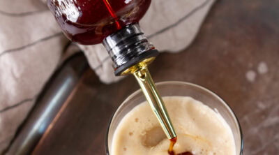 square crop pouring simple syrup into an iced latte.