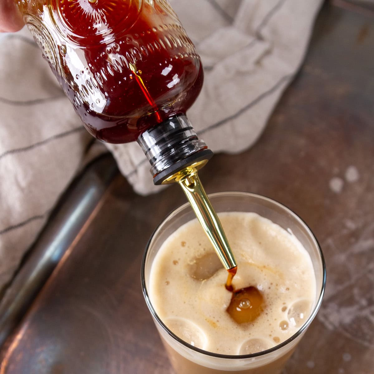 square crop pouring simple syrup into an iced latte.