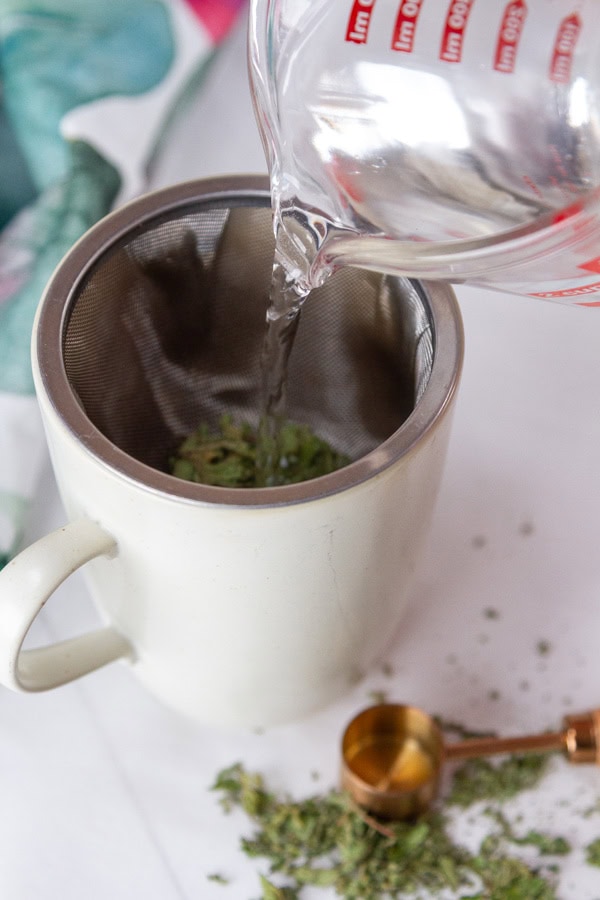 a mug with a metal strainer and tea in the strainer, water being poured in the mug.
