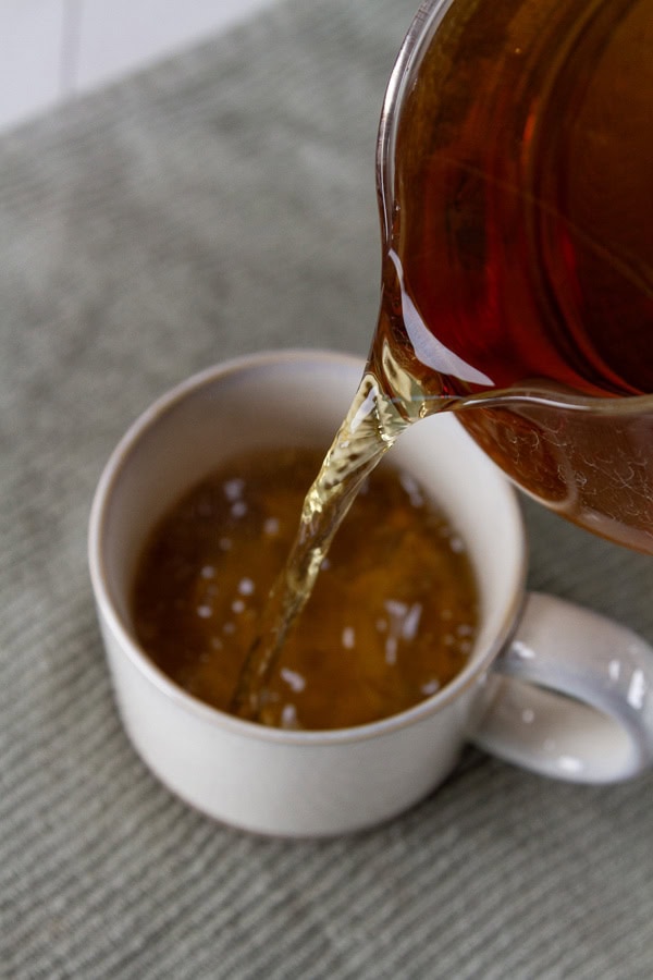 pouring brewed tea into a white mug.