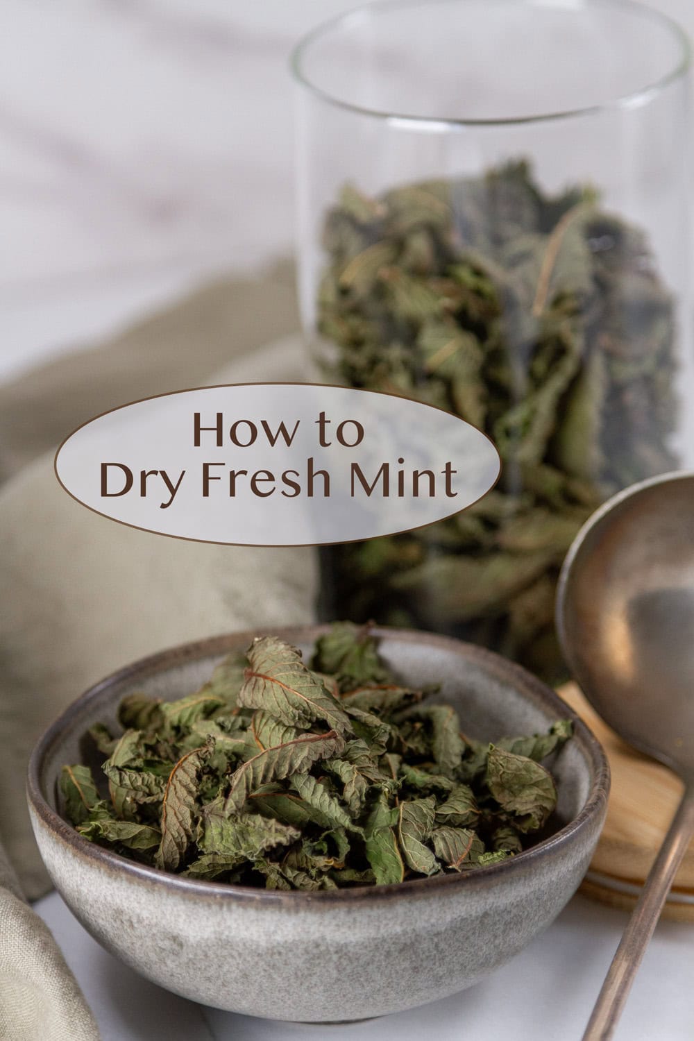 a small bowl of dried mint in front of a glass container full of dried mint.