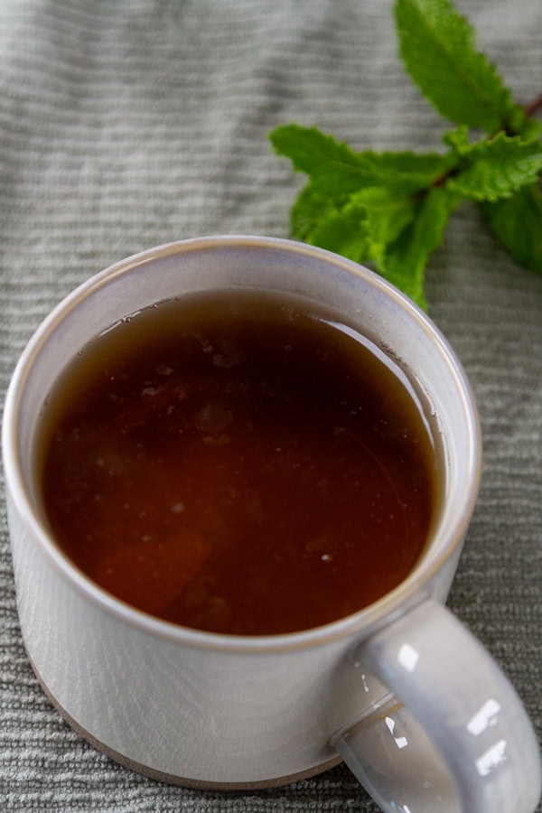 brewed mint tea in a white mug with fresh mint next to the mug.