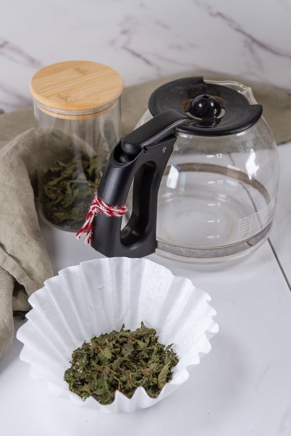 a coffee filter with mint tea in it, an empty coffee pot, and a canister of mint tea.